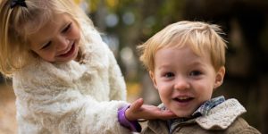 toddler girl touching and looking at chin of toddler boy smiling