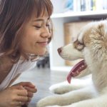 young woman with short brown hair lying on ground looking at husky puppy