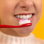 A woman pointing to her clean, white smile while holding a yellow toothbrush