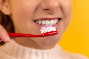 A woman pointing to her clean, white smile while holding a yellow toothbrush