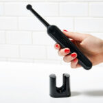 Black electric toothbrush held in a person's hand against a white background.