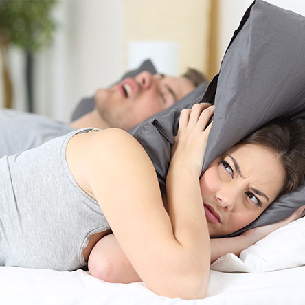 woman holding a pillow over her ears because of her husband's loud snoring