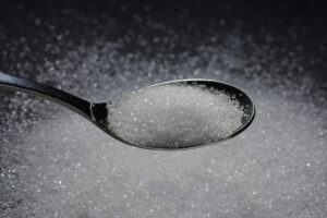 A metal spoon holding processed white table sugar over a dark background